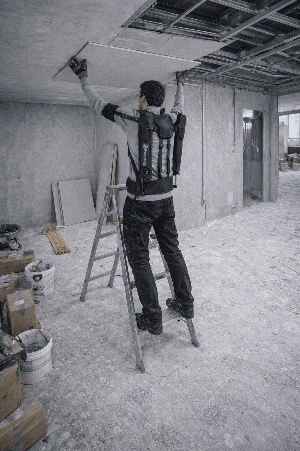 Plaquiste équipé d’un exosquelette réalisant une tâche bras levés sur échasses