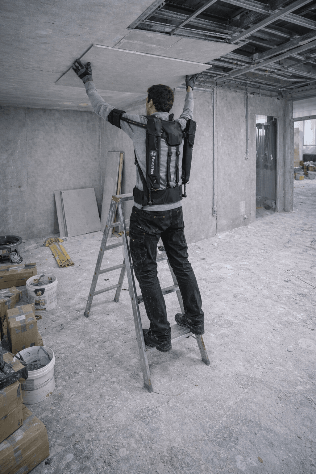 Plaquiste équipé d’un exosquelette réalisant une tâche bras levés sur échasses